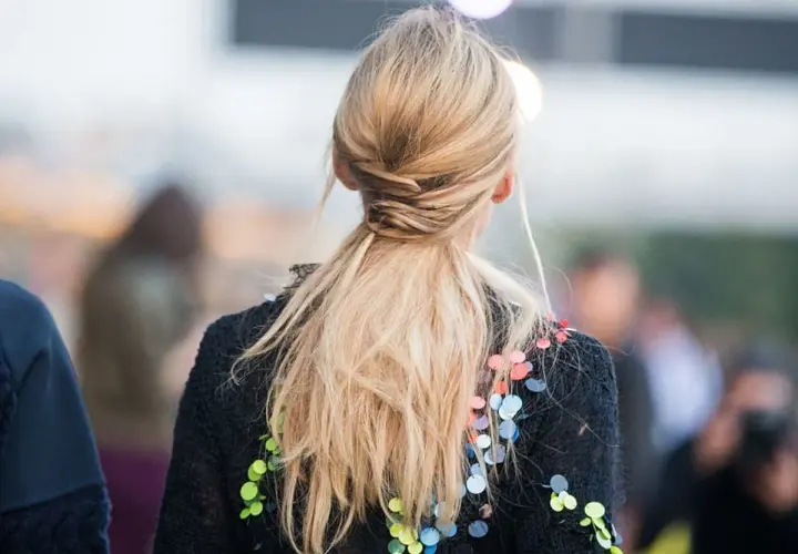 Elegancka fryzura na wesele: blond włosy spięte w niski, luźny warkocz z ozdobnymi pasemkami.