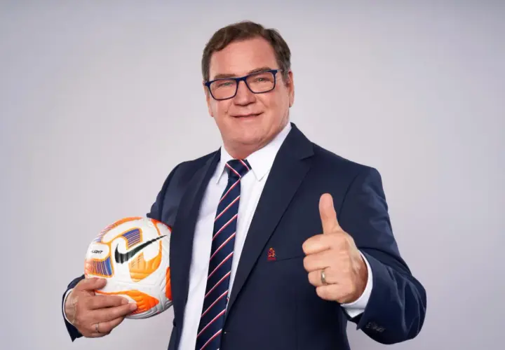 Uśmiechnięty mężczyzna w garniturze, z piłką w ręku i kciukiem w górze. Wygląda jak trener reprezentacji Polski, gotowy do akcji.