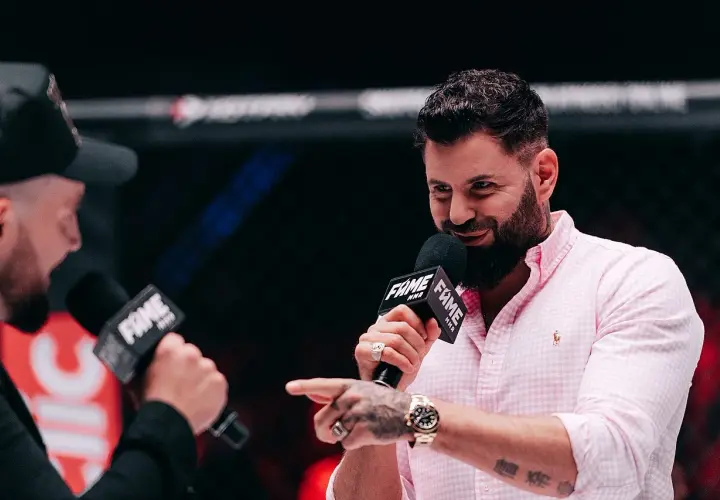 Wojtek Gola, znany z FAME MMA, udziela wywiadu. Uśmiechnięty, w różowej koszuli, z mikrofonem w dłoni.