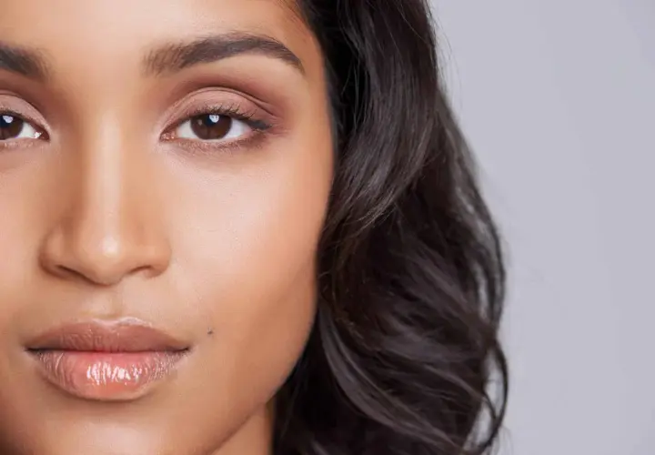 Un grain de beauté discret, comme un petit tatouage naturel, orne la joue d'une jeune femme aux yeux expressifs et aux lèvres brillantes.
