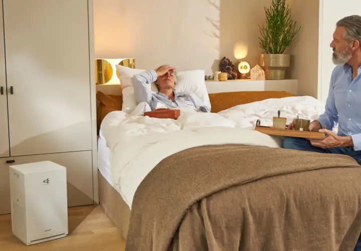 Hombre cuida a mujer enferma en cama. Purificador de aire Daikin al lado, mejorando la calidad del aire iaq.