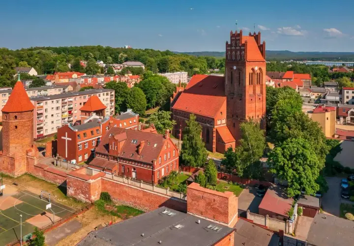 Zamek krzyżacki w Lęborku, z charakterystyczną wieżą i ceglaną architekturą, otoczony zielenią i miejską zabudową.