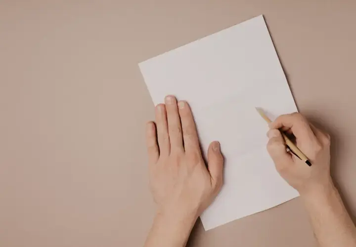 Ręce piszą list motywacyjny po angielsku na białej kartce.