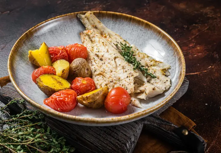 Delicioso abadejo a la plancha servido con patatas asadas y tomates cherry.