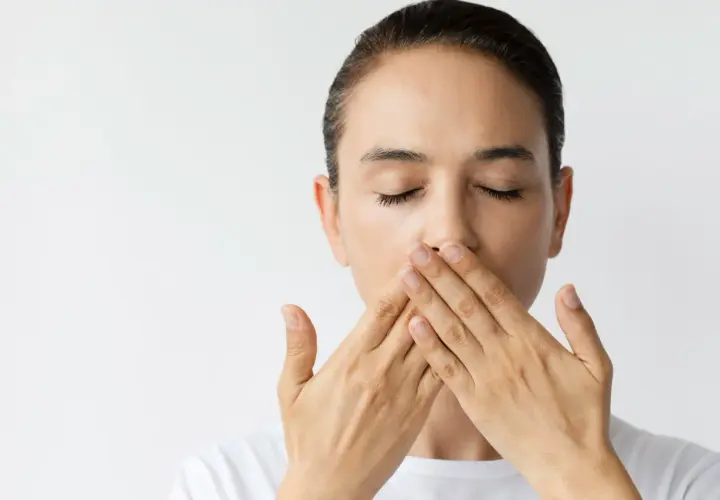 Donna con occhi chiusi copre la bocca con le mani, un'espressione di **bocca amara** sul volto.