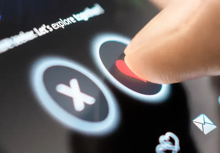 Palec dotyka serca na ekranie telefonu, wybierając potencjalną randkę. Aplikacje randkowe na telefon ułatwiają poznawanie nowych ludzi.