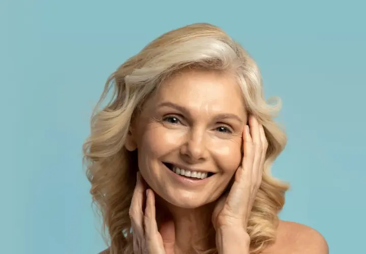 Uśmiechnięta kobieta z blond włosami, której skóra lśni dzięki olejkowi kameliowemu.