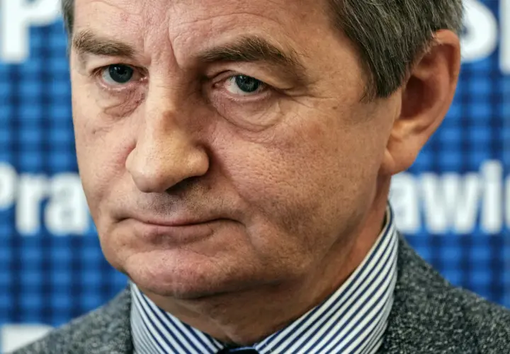 Mężczyzna w garniturze, w tle niebieska krata z białymi literami. Czy to on wyjaśnia, dlaczego posłowie PiS zostali oskarżeni o nadużywanie lotów rządowych?
