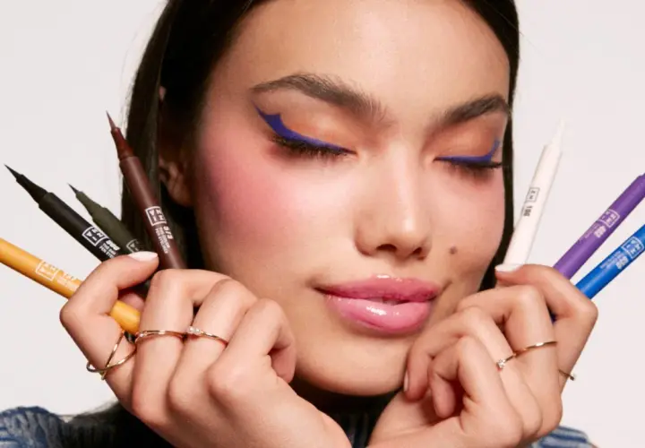 Mujer con delineado azul vibrante y varios eyeliners de colores en sus manos. Descubre qué es el eyeliner perfecto para ti.