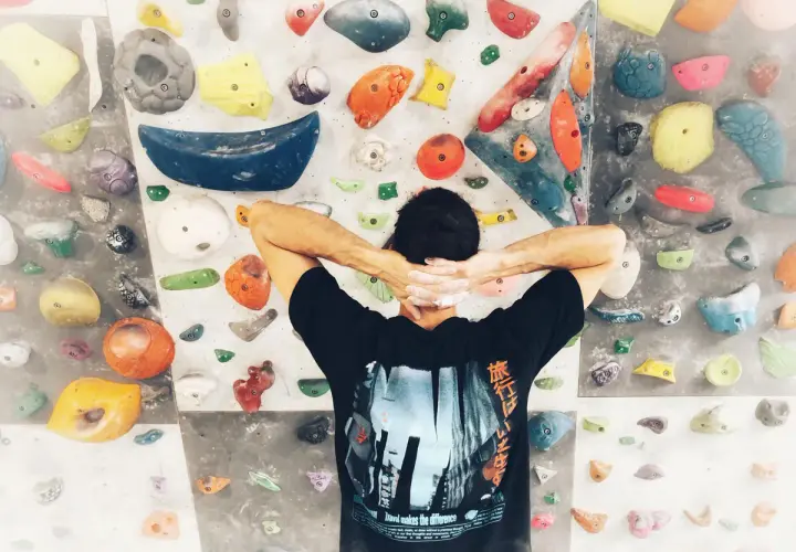 Wspinaczka bouldering na kolorowej ściance. Mężczyzna z rękami za głową, przygotowuje się do pokonania trudnej trasy.