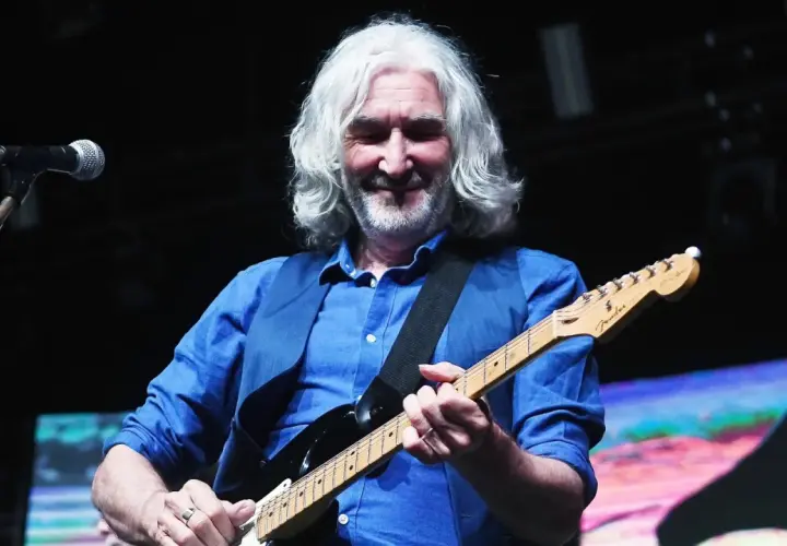 Muzyk z siwymi włosami gra na gitarze, przypominając legendarne utwory Dire Straits.