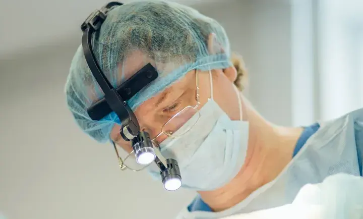 Kirurg med lupp och mask utför buccal fat removal i Sverige.