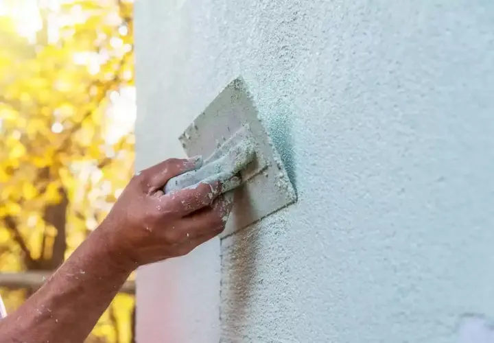 Ręka fachowca wygładza świeży tynk gąbką. Gąbkowanie tynku po jakim czasie daje najlepszy efekt?