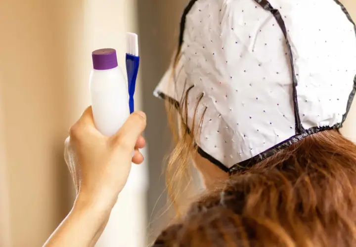 Persona se prepara para hacerse mechas en casa. Sostiene un aplicador y un gorro para el cabello.