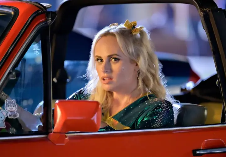 Dziewczyna w stroju cheerleaderki, z błyszczącymi akcentami, jedzie czerwonym kabrioletem. To jej powrót do liceum po latach.