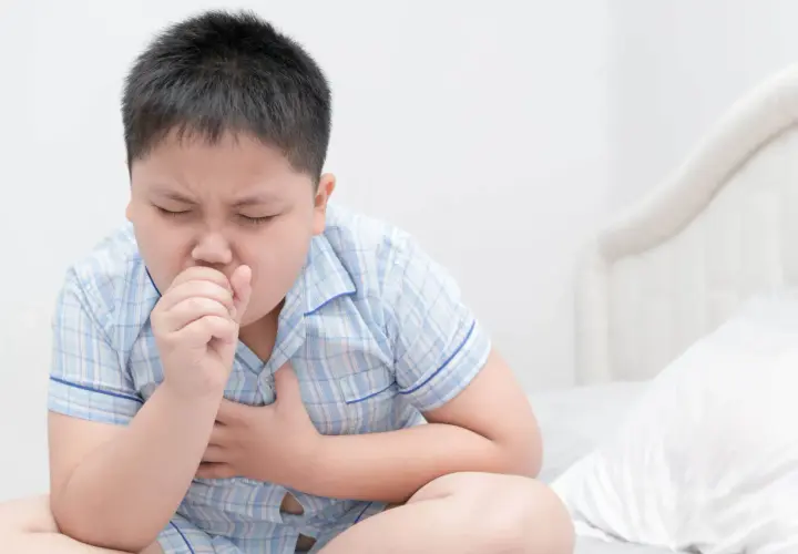 Niño con tos, con la mano en la boca y el pecho. ¿Cuándo preocuparse por tos en niños?