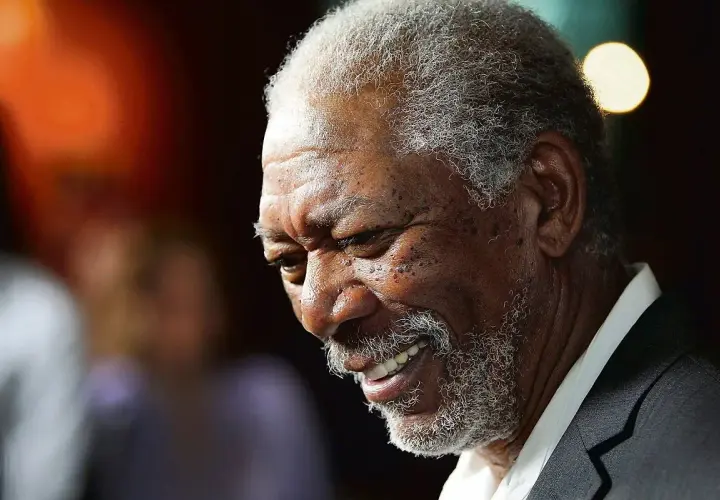 Uśmiechnięty aktor murzyn, Morgan Freeman, z siwą brodą i kręconymi włosami, w garniturze.