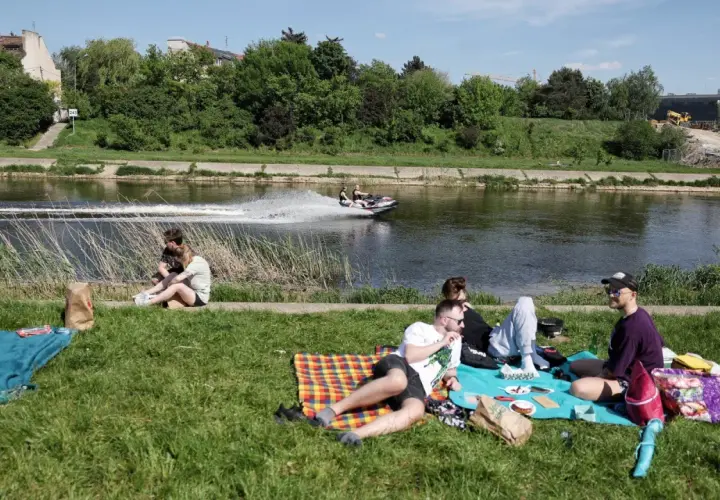 Majówka nad rzeką w Polsce: ludzie odpoczywają na trawie, a na wodzie ścigają się skutery wodne. Idealne miejsce, by spędzić wolny czas.