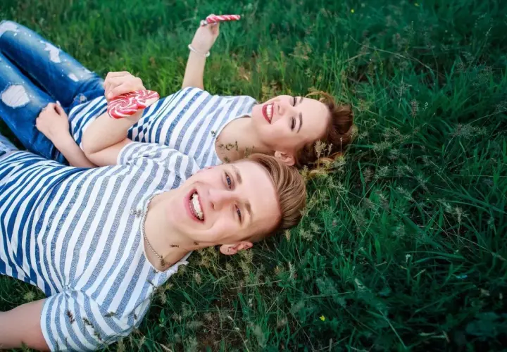 Para, która leży na trawie, trzymając lizaki. Ich uśmiechy sugerują, że mają otwarty związek, co to znaczy?