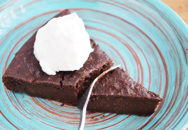 Pyszny brownie z cukinii codziennie fit, podane z bitą śmietaną na turkusowym talerzu.