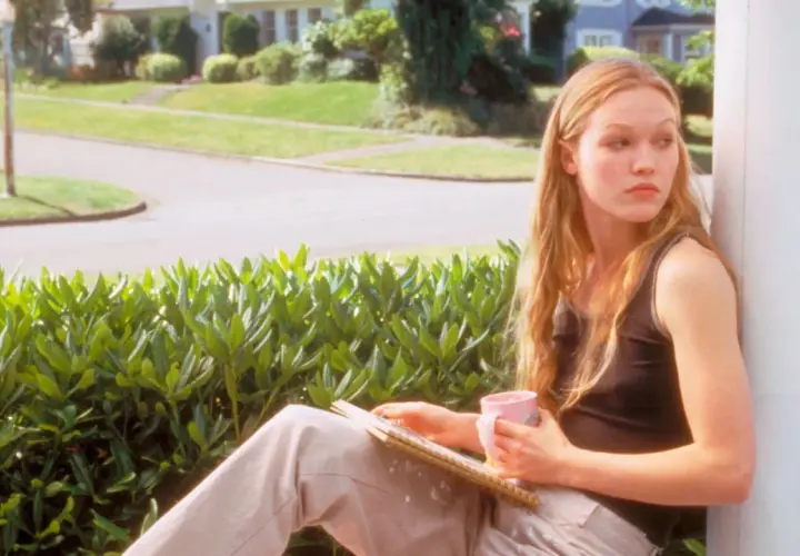 Kat Stratford, protagonista di "10 cose che odio di te trama", pensierosa con una tazza rosa e un quaderno.