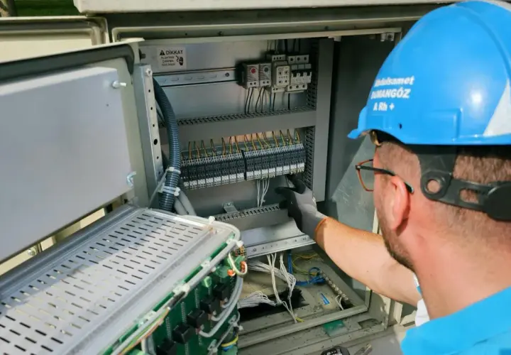 Elektryk w niebieskim kasku pracuje przy panelu sterowania, przygotowując oświadczenie o gotowości instalacji przyłączanej.