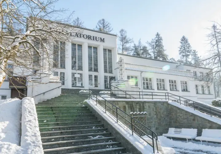 Zimowy dzień w Szczawnicy. Biały budynek sanatorium z napisem "Sanatorium" i schody pokryte śniegiem. Idealne miejsce na relaks w termach.