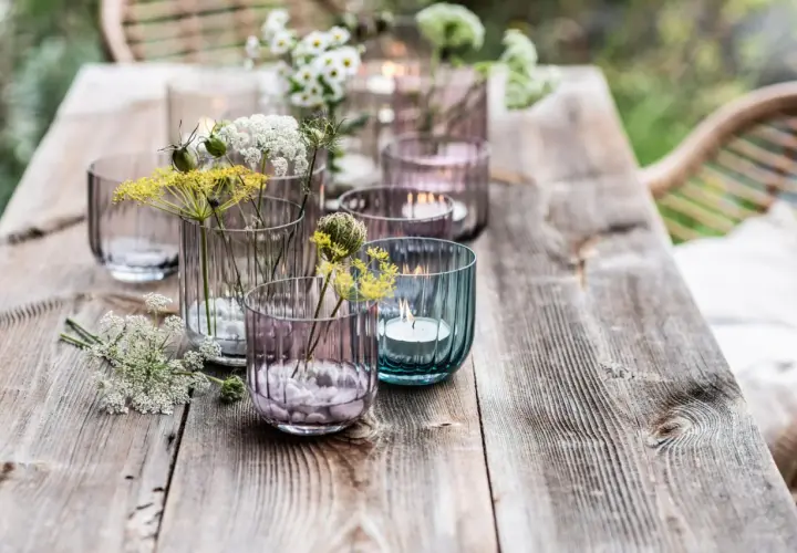 Romantische deko gartentisch mit Blumen und Kerzen in bunten Gläsern.