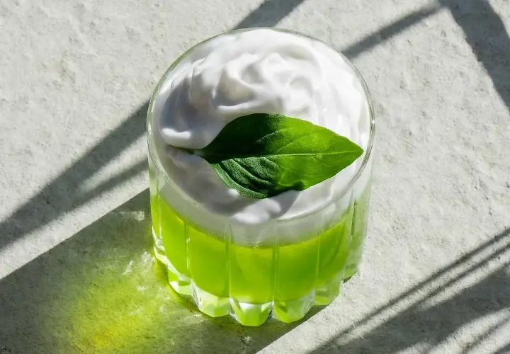 En grön thai basil drink med vitt skum och ett basilika-blad.