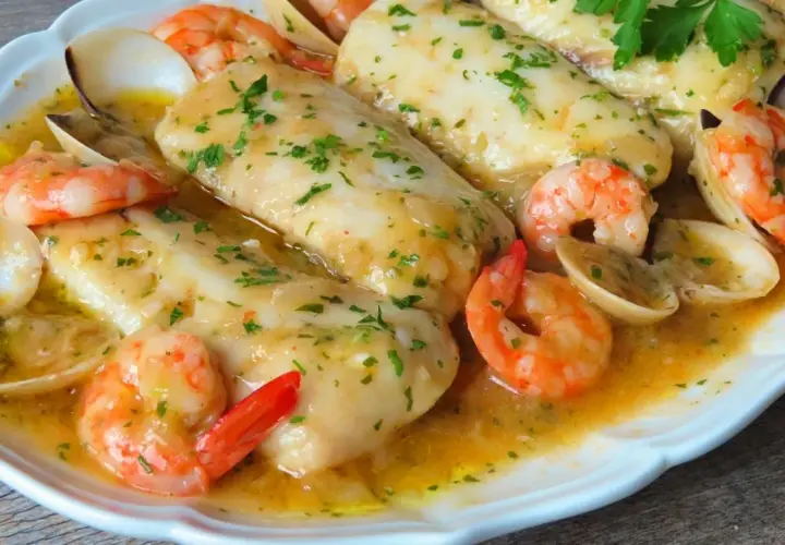 Merluza a la marinera con patatas, gambas y almejas en una salsa dorada.
