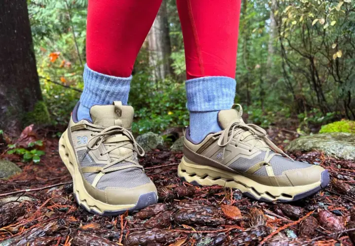 These tan hiking shoes with grey socks and red leggings are perfect for exploring a forest floor covered in pinecones.