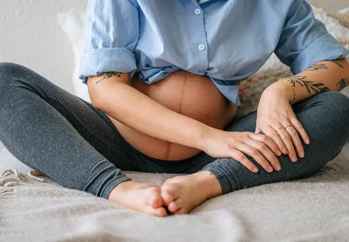 Donna incinta con pancia visibile, seduta a gambe incrociate, che si tiene le gambe, forse per alleviare il mal di gambe in gravidanza.