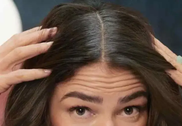 Mujer se toca el cabello oscuro, mostrando cómo disimular las canas en la raya.