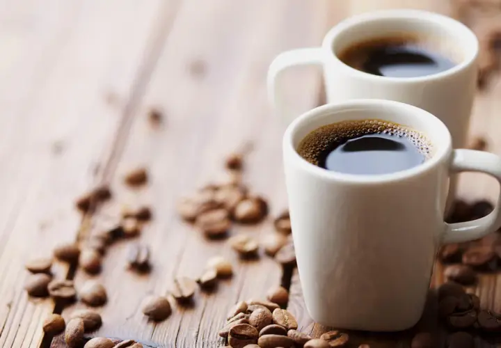 Dwa białe kubki z aromatycznym espresso na drewnianym blacie, otoczone ziarnami kawy. Zastanawiasz się, ile mg kofeiny ma espresso?