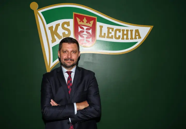 Marcin Kaczmarek, trener, stoi przed zieloną ścianą z logo Lechii Gdańsk.
