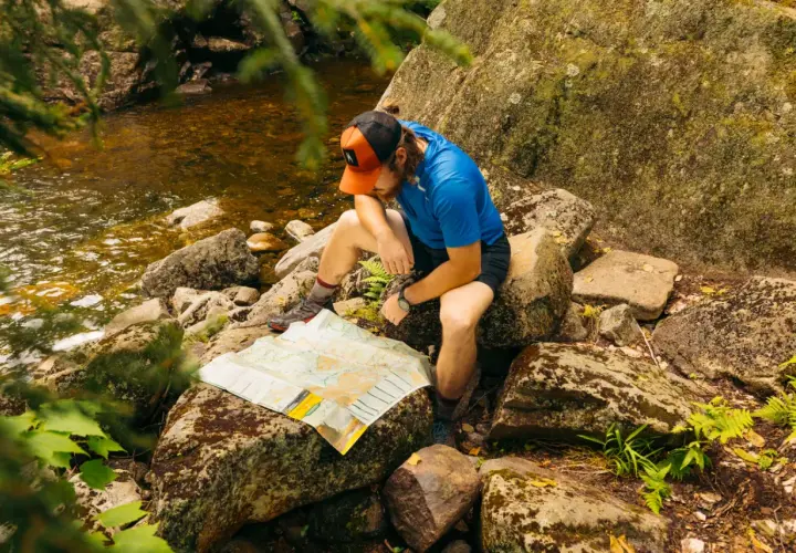 A hiker consults a map by a stream, perhaps planning his next move after some bushwhacking.