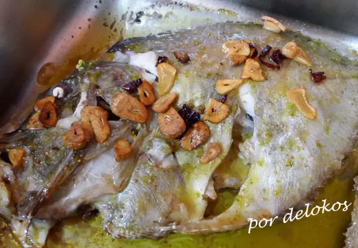 Un delicioso san martiño pescado al horno con ajo laminado y hierbas verdes, bañado en su jugo.
