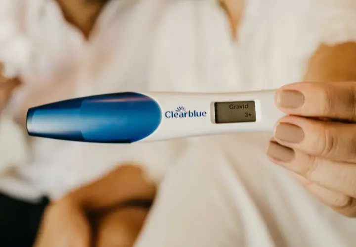 En kvinna håller en graviditetstest som visar "Gravid 3+". Kanske är det gravid andra barnet symtom som hon känner av.