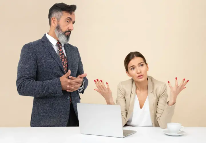 Un collega che vuole comandare, con un'espressione autoritaria, parla con una collega che sembra confusa e frustrata.
