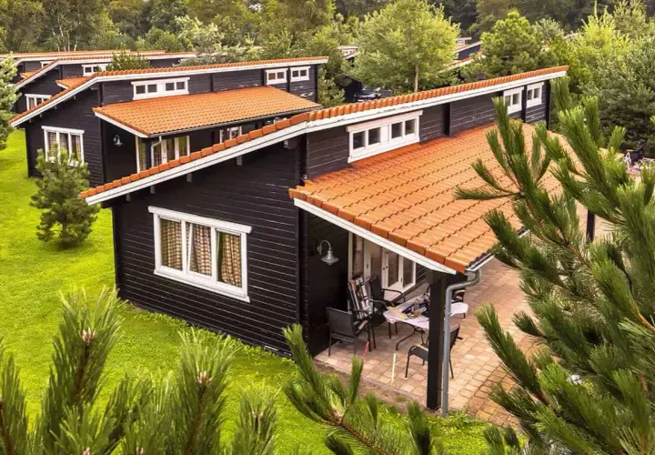 Czarny bungalow z pomarańczowym dachem, otoczony zielenią. Idealne miejsce na wakacje, co to za urok!