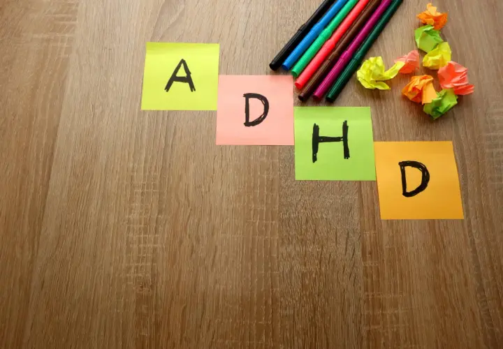 Kolorowe karteczki z literami A, D, H, D układają się w słowo "ADHD". Obok leżą pisaki i pomięte kartki.