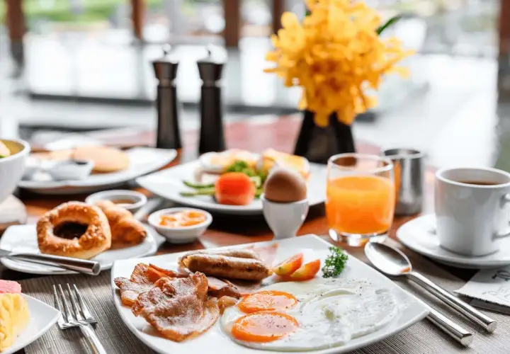 Desayuno abundante con huevos, salchichas, tocino y zumo de naranja, perfecto para tus viajes fin de semana baratos todo incluido.