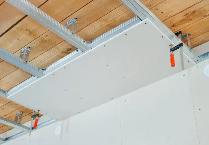 Installation d'un faux plafond en plaques de plâtre pour l'isolation phonique plafond appartement. Structure métallique fixée au plafond bois.