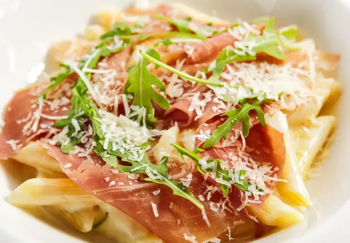 Penne z kremowym sosem, szynką parmeńską, rukolą i parmezanem. Pyszne danie, które zachwyci każdego smakosza.
