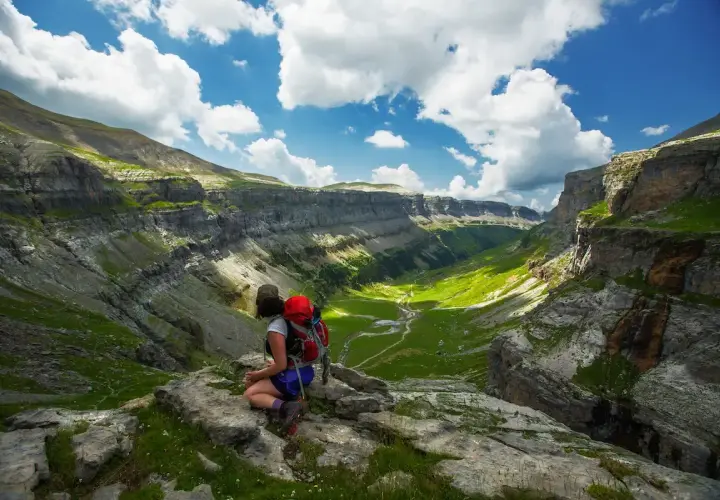 Senderista contempla el impresionante valle de Ordesa en Monte Perdido, Huesca, bajo un cielo azul con nubes algodonosas.