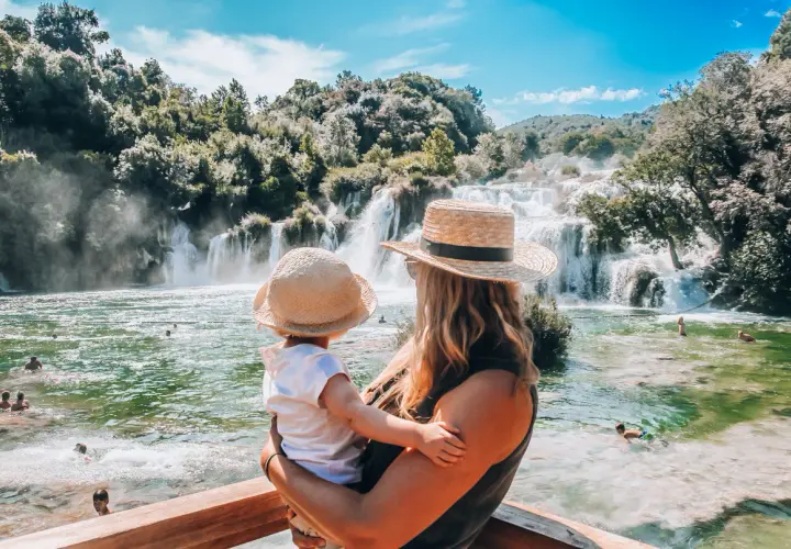 Mama z dzieckiem podziwia piękne wodospady Krka. Woda w rzece jest krystalicznie czysta, a wokół bujna zieleń.