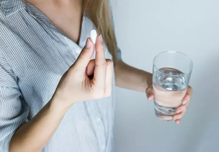 Donna tiene una pillola, forse un antibiotico per denti e gengive, accanto a un bicchiere d'acqua.
