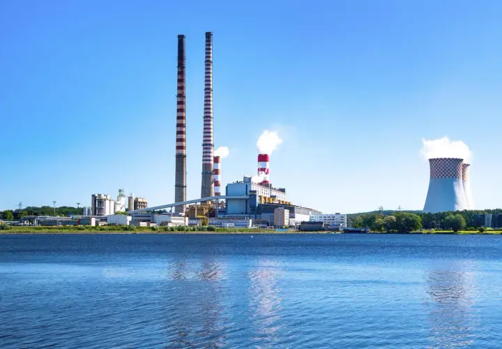 Elektrownia z kominami i chłodniami, odbijająca się w wodzie.