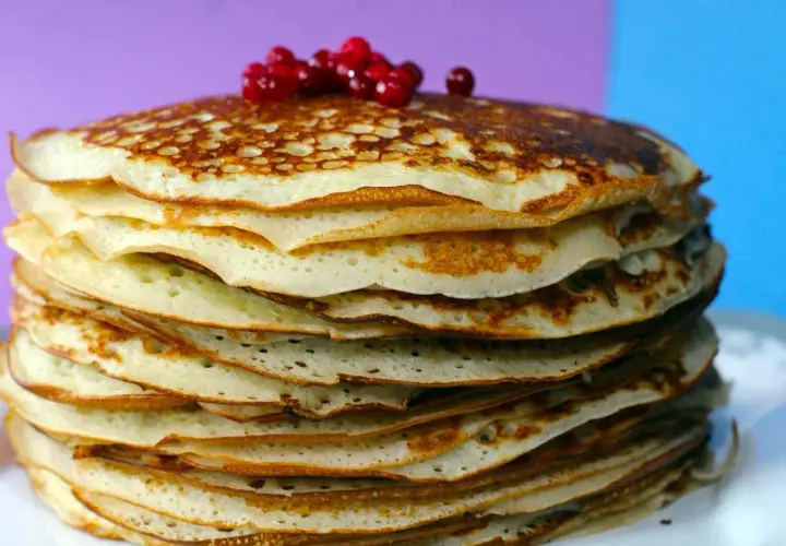Pila di pancake senza farina, dorati e soffici, guarniti con bacche rosse.
