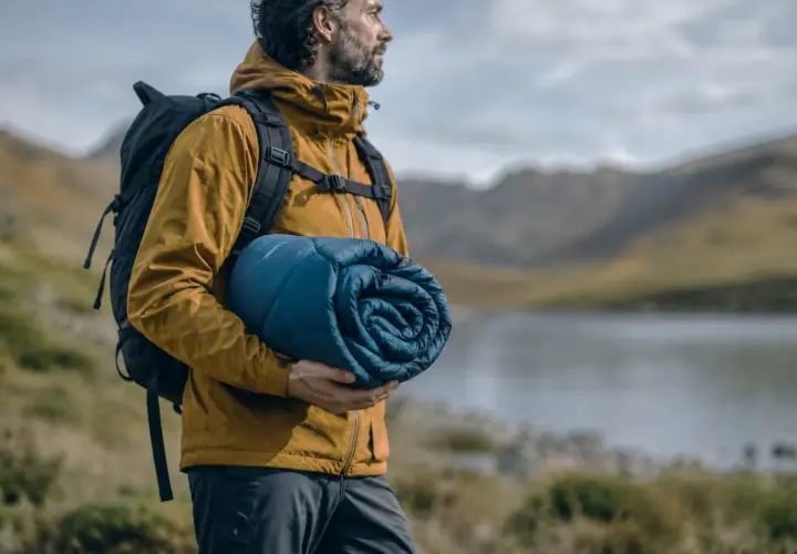 Hombre con mochila y saco de dormir enrollado, listo para elegir su aventura.